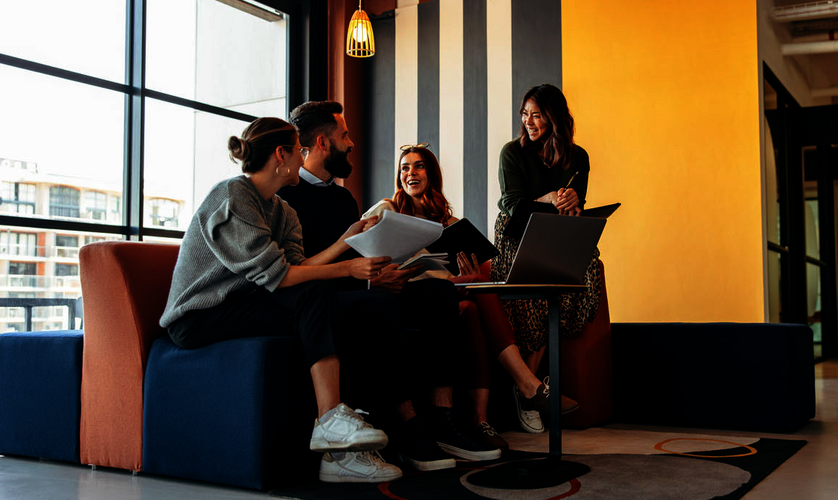Drei junge Frauen und ein Mann sitzen auf einem Sofa vor einem Laptop.