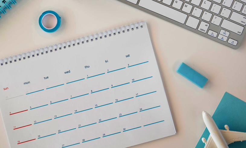 A vacation planner calendar lies on a desk next to a keyboard, a tape and a little airplane